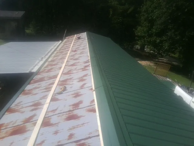 Old rusted panels beside newly installed green metal roofing — Wind Damage Roof Repair by Roofing Brothers in Ryegate