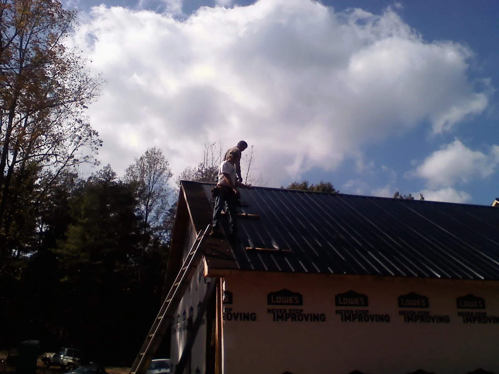 Roofer fastening dark metal panels high against a cloudy sky, from a Roof Inspection job in Ryegate