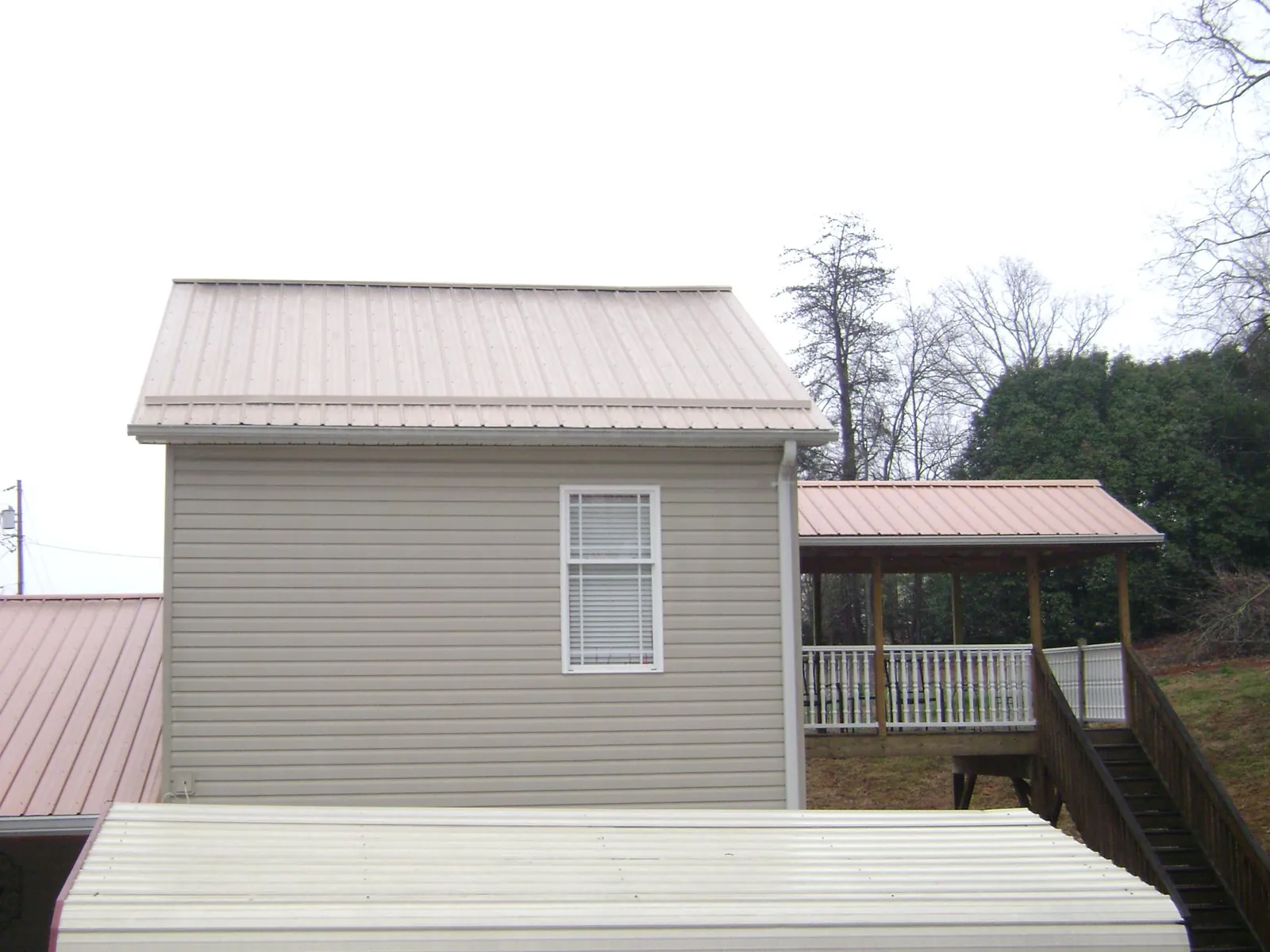 Tan metal roofs on a two story addition and attached porch, from a Roof Replacement job in Ryegate